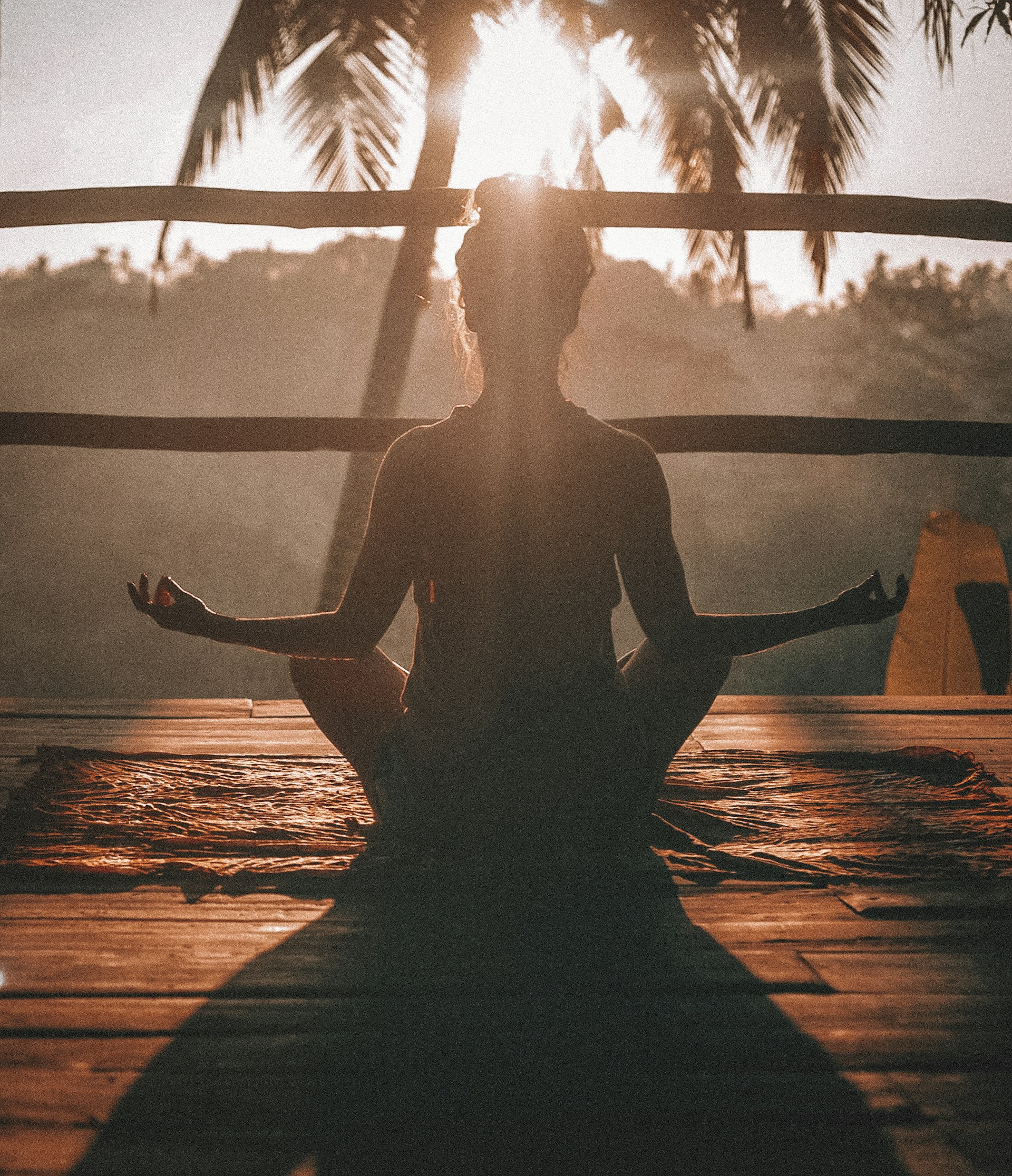 Woman doing yoga meditation under palm trees at sunset